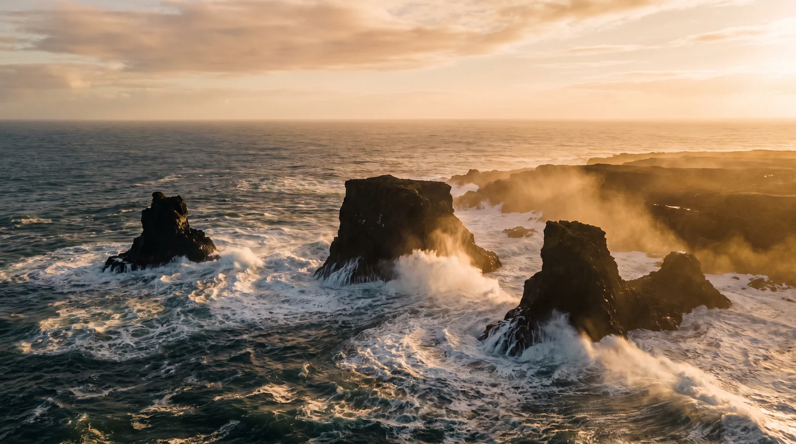 Waves breaking against black sea stacks at golden hour