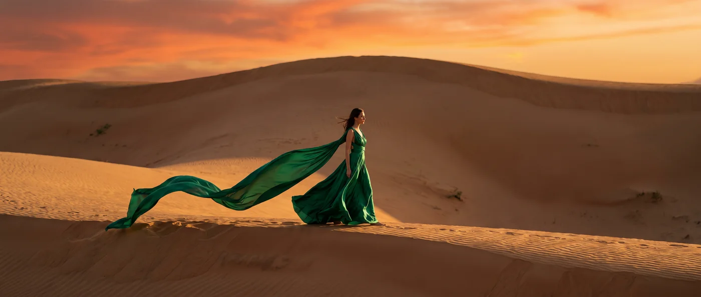 A model in an emerald silk gown walking a dune ridge at sunset