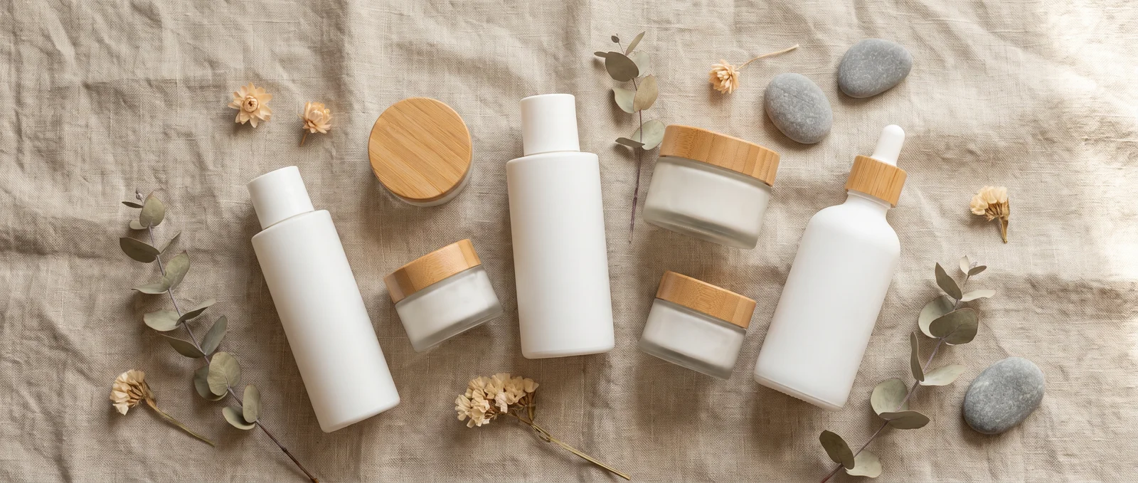 A minimalist skincare set laid out on linen with dried flowers and pebbles